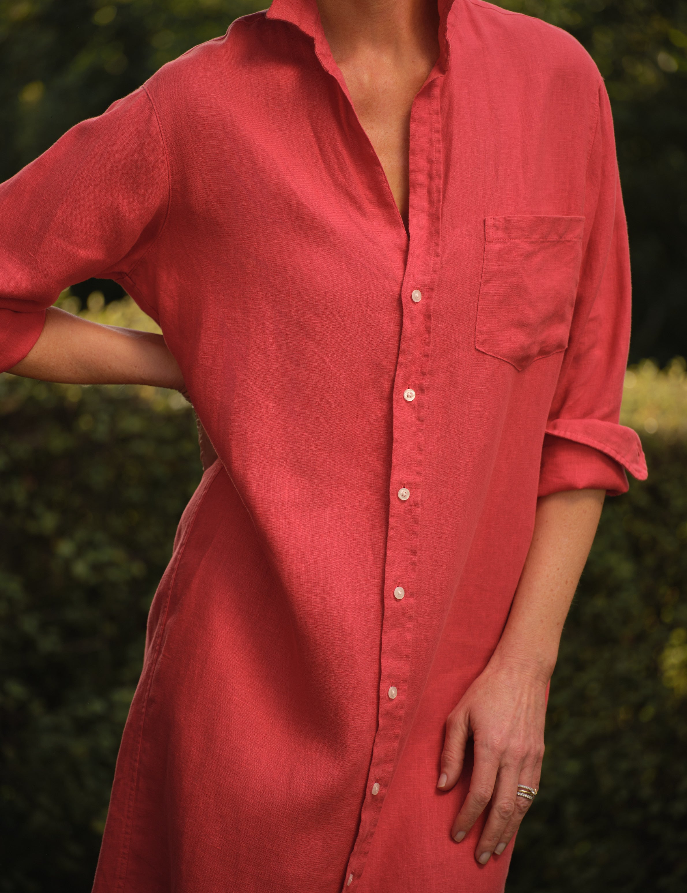 Person wearing a red dress with rolled-up sleeves against a blurred green background, view 3