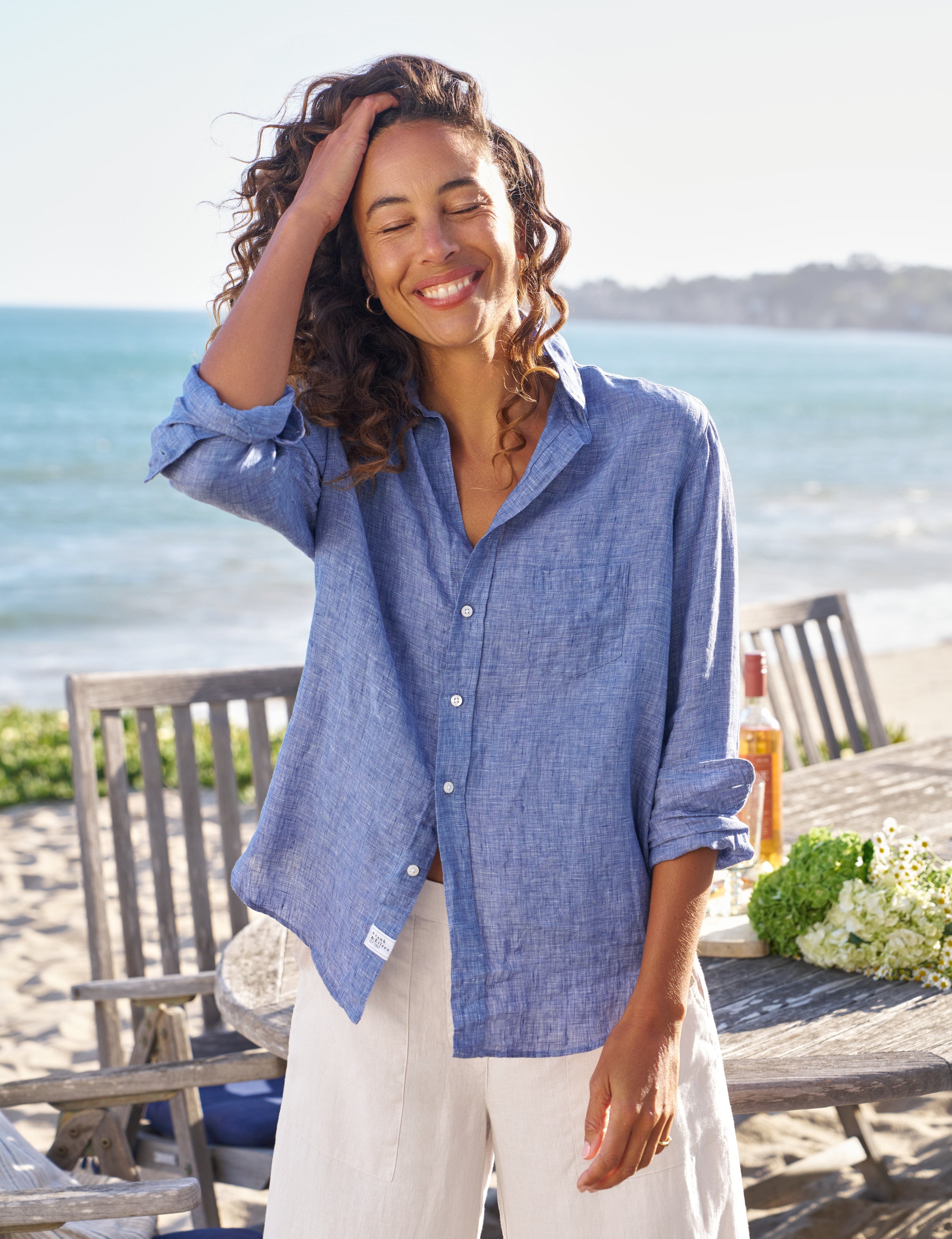 Woman wearing a blue shirt and white pants standing on a beach with ocean view., front view