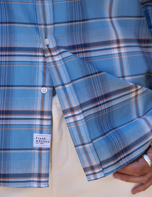 Close-up of a blue plaid button-up shirt with white and brown stripes, featuring a visible 'Frank & Eileen' label patch and a hand holding the cuff., view 3