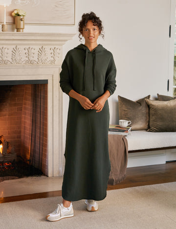 Person wearing a green dress standing in a living room with a fireplace and sofa.