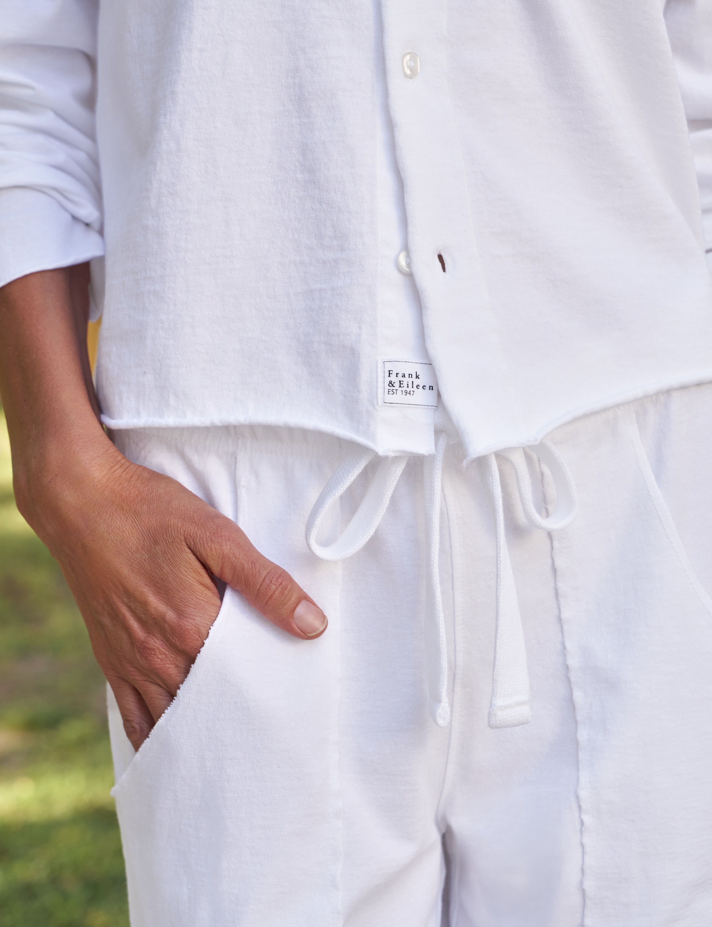 Person wearing a white shirt and pants with a brand label, standing outdoors., view 3