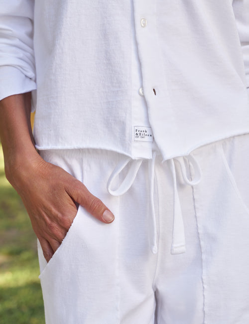 Person wearing a white shirt and pants with a brand label, standing outdoors., view 3