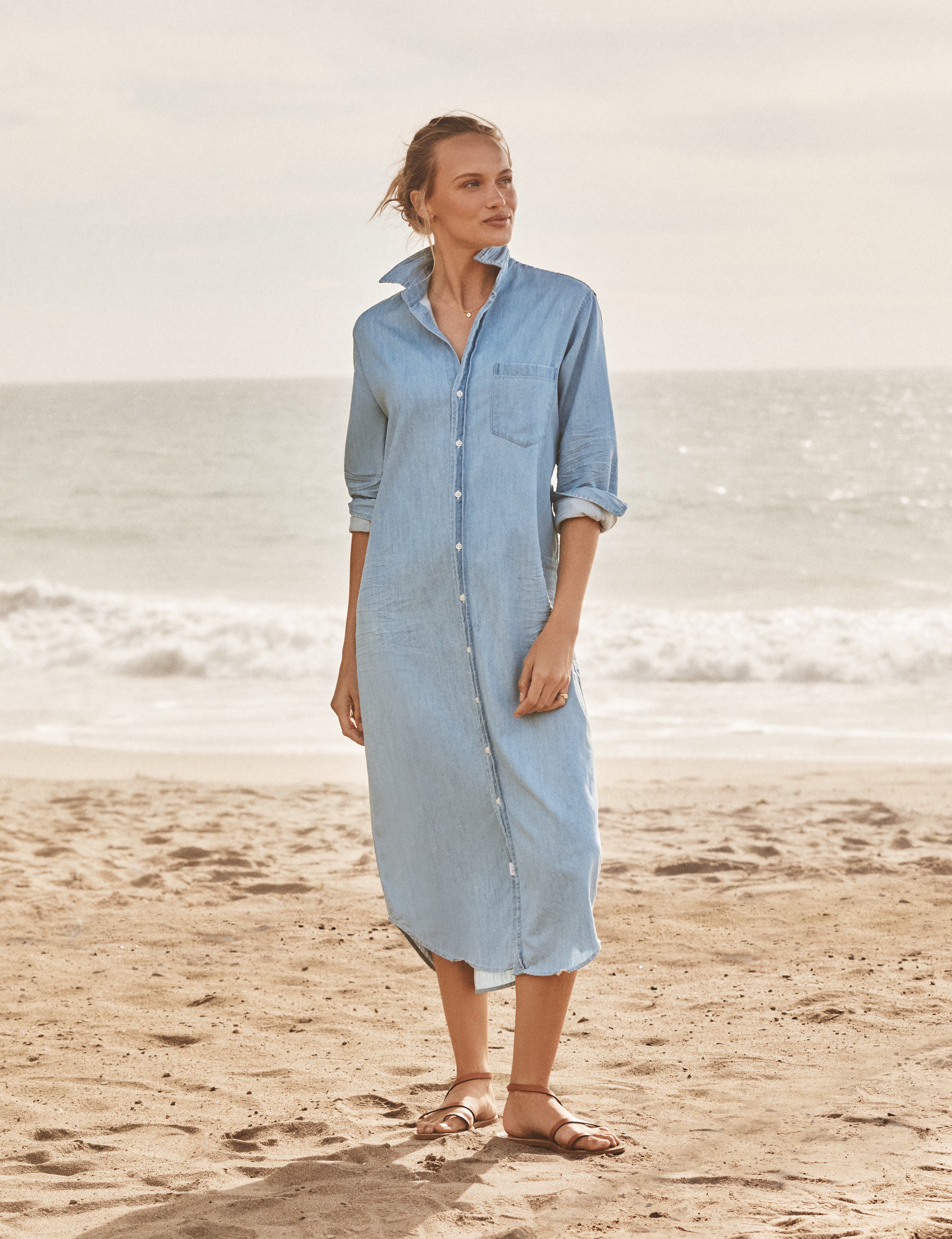 Woman wearing a light blue dress standing on a beach with ocean waves in the background, front view
