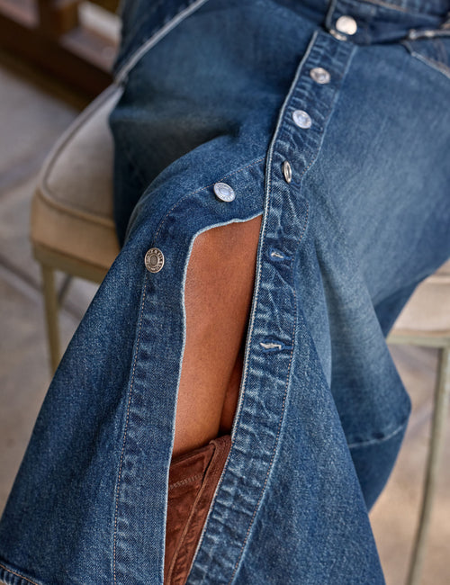 Close-up of a person wearing a blue denim skirt with a brown suede boots, seated on a chair., view 4