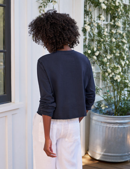 Person wearing a navy long-sleeve shirt and white pants standing in front of a white building with floral decorations., alternate view