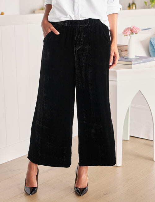 Person wearing black wide-leg pants and a white shirt in a minimalistic room., front view