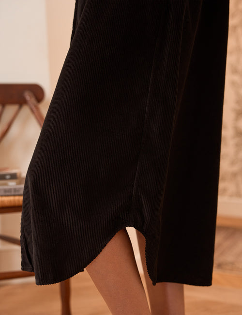 Close-up of a black corduroy dress with a side slit, worn by a model in a warm indoor setting., view 3