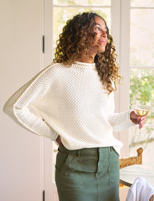 Woman in a white sweater and green skirt holding a glass of wine indoors., view 3