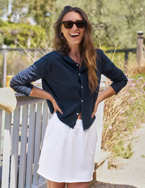 Woman wearing a navy blue cardigan and white skirt outdoors, view 5