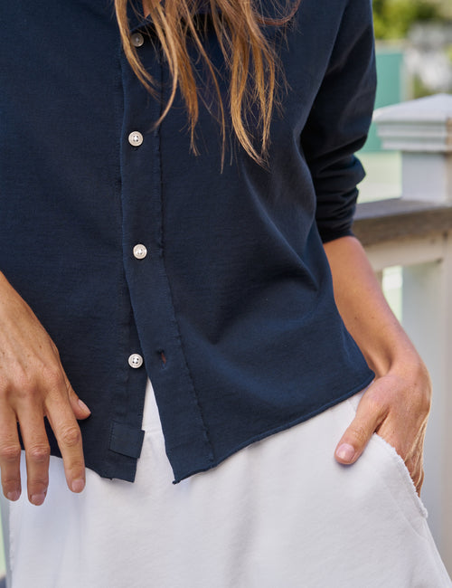Person wearing a navy button-up cardigan and white skirt with a blurred background, view 4