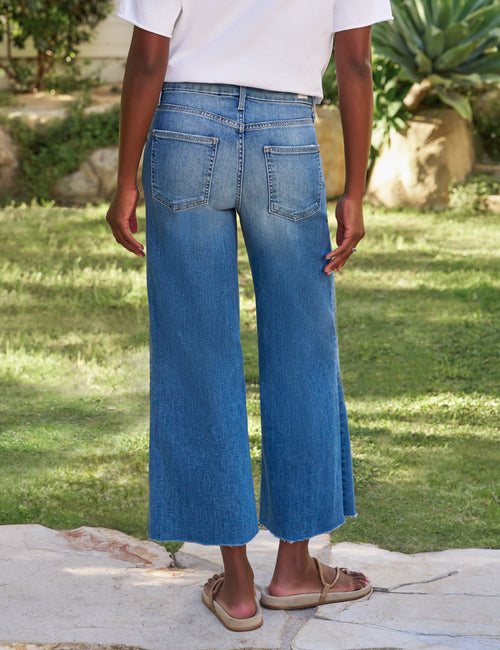 Person wearing blue jeans standing on a stone path with grass and plants in the background, alternate view