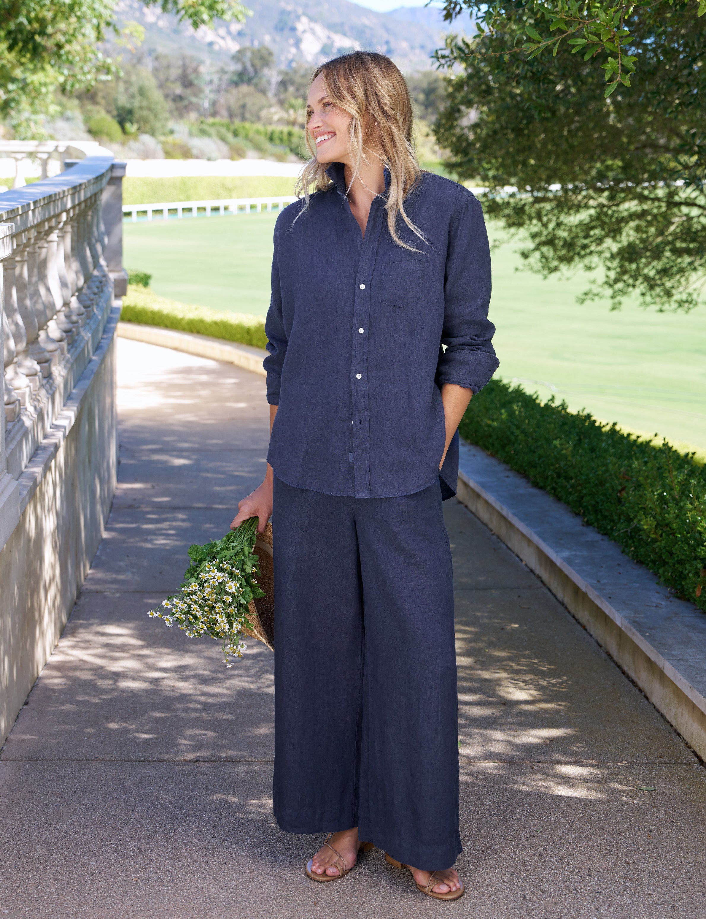 Woman in navy blue outfit standing outdoors with greenery in the background