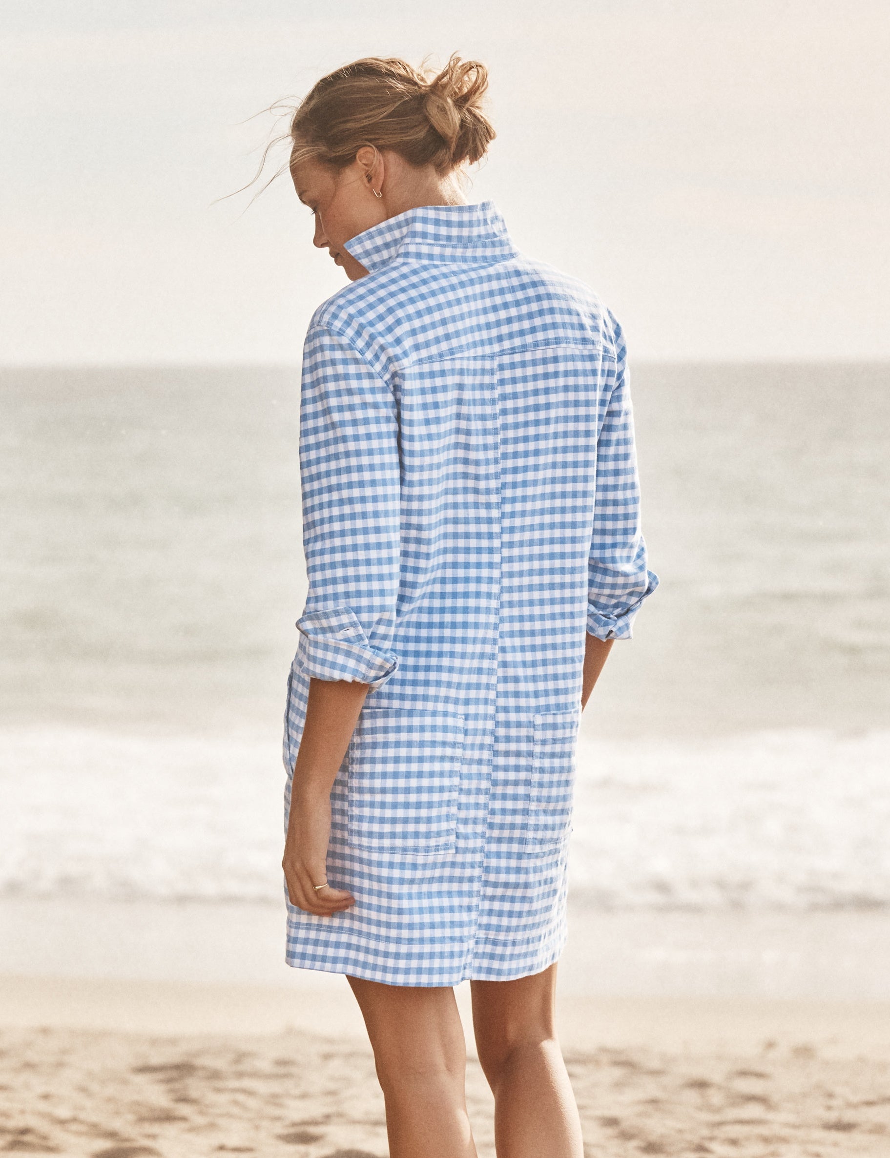 Woman wearing a blue and white checkered dress on a beach., alternate view