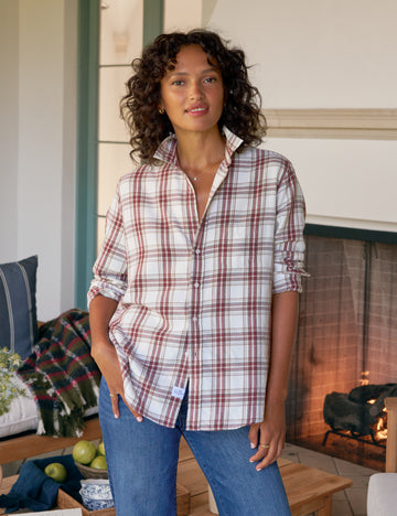 Woman wearing a plaid shirt and jeans standing in a cozy living room.