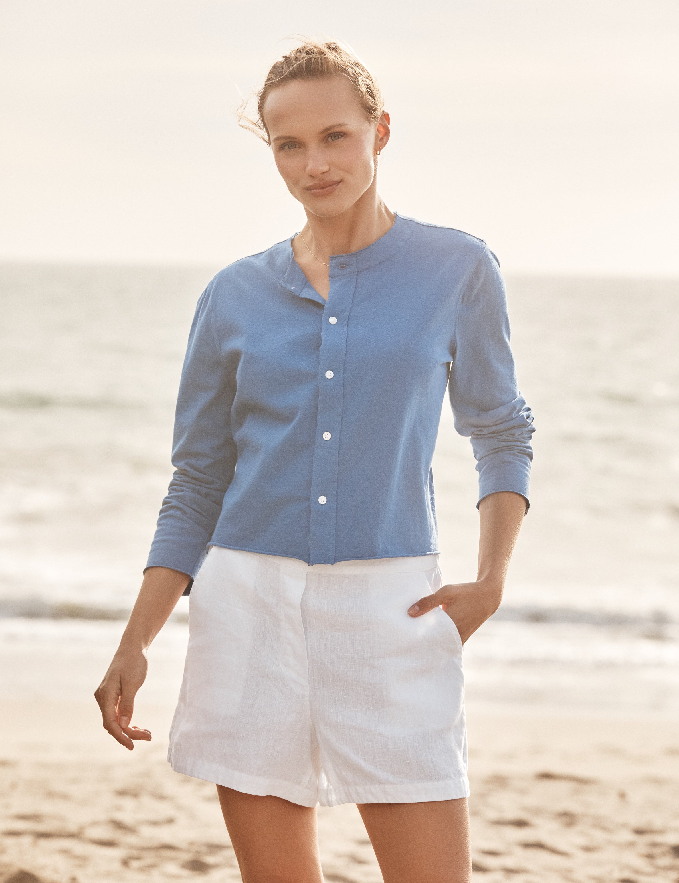 Woman wearing a blue shirt and white shorts standing on a beach., view 3