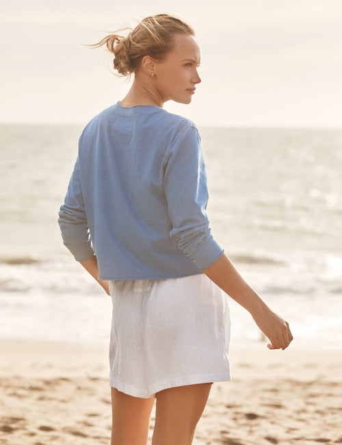 Woman in a blue sweater and white skirt standing on a beach., view 4