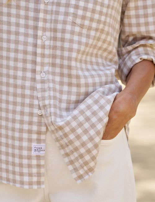 Close-up of a person wearing a beige and white gingham check button-up shirt with cream pants, showing a small 'Frank & Eileen' brand label near the pocket., view 3