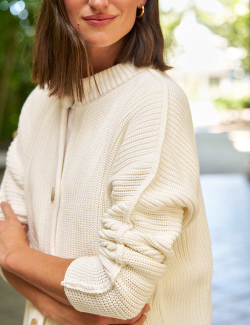 A woman wearing a cream-colored, textured knit cardigan sweater with a button-front closure and gathered sleeves, photographed outdoors with a blurred background., view 3