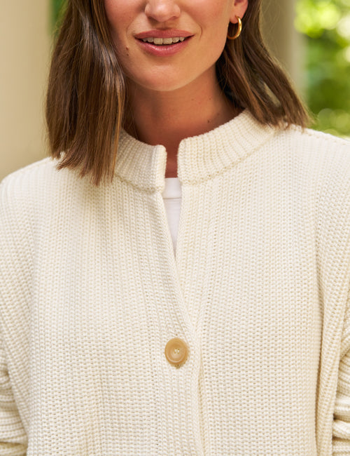A close-up of a woman wearing a cream-colored textured knit cardigan with a single tan button, styled over a white top., view 4