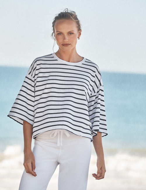 Woman wearing a striped shirt and white pants standing on a beach., front view