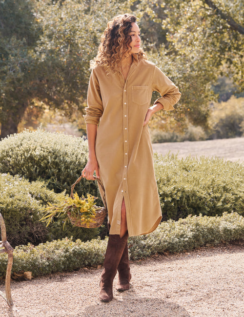 Woman in a beige dress standing outdoors with greenery in the background, front view