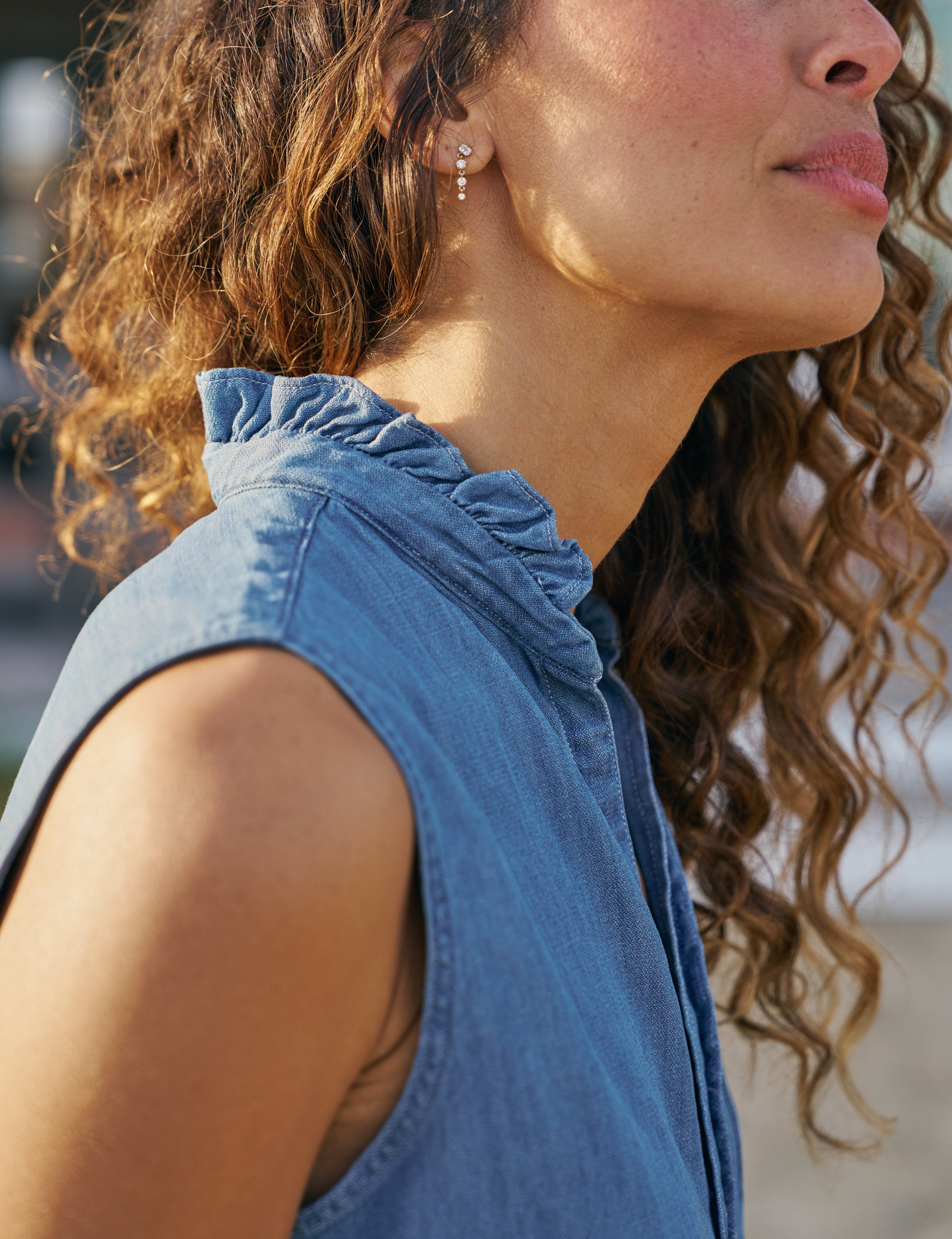 Woman wearing a blue sleeveless top with ruffled collar, close-up of neck and shoulder., view 3