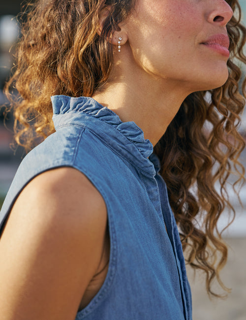 Woman wearing a blue sleeveless top with ruffled collar, close-up of neck and shoulder., view 3