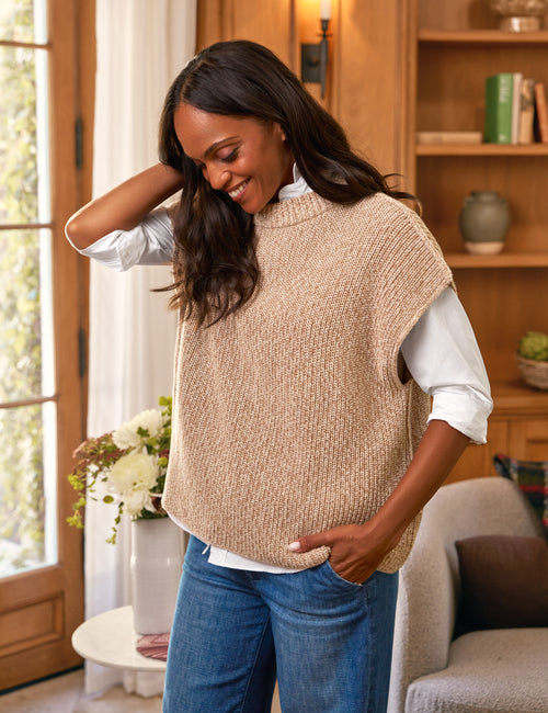 Woman wearing a beige knitted vest in a home setting, front view