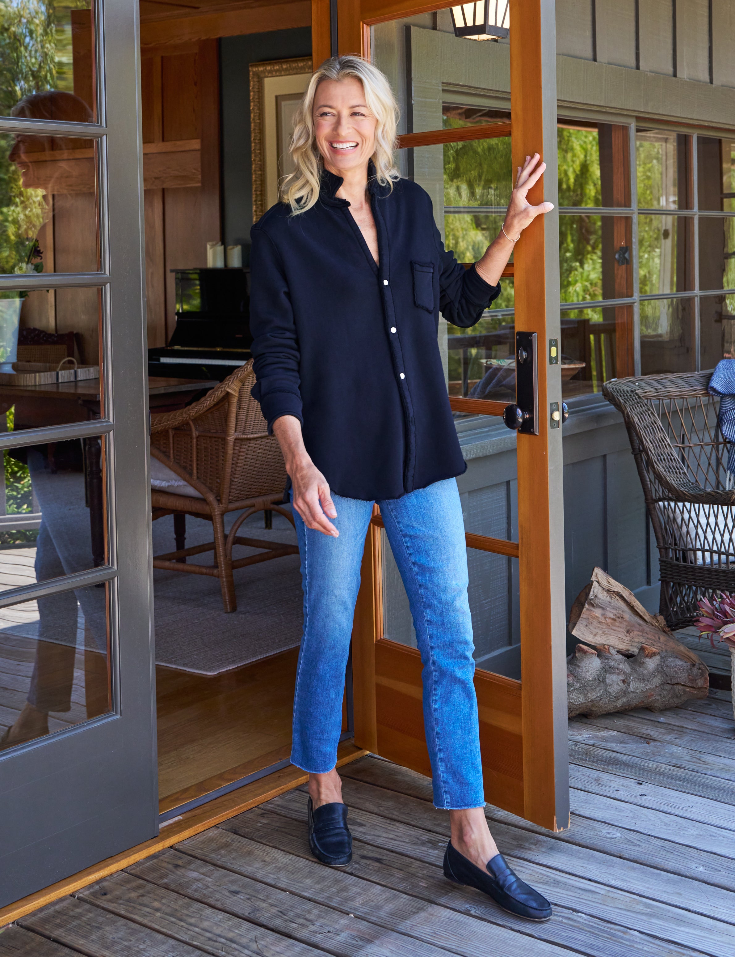 Woman standing in a doorway wearing a navy shirt and blue jeans, smiling.