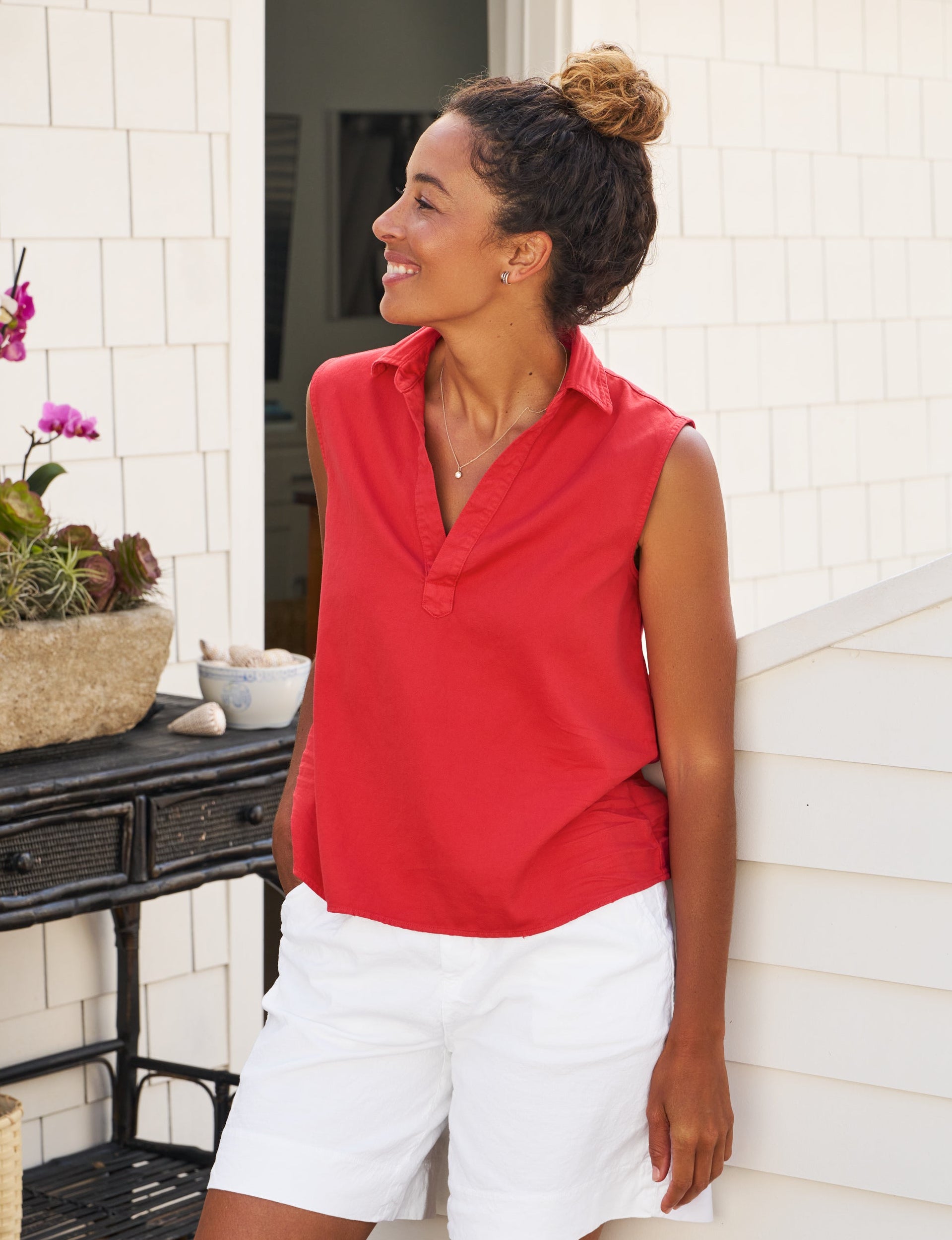 Woman in a red shirt and white shorts standing on a porch., front view