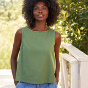 Woman wearing a green sleeveless top and blue jeans standing outdoors with trees in the background