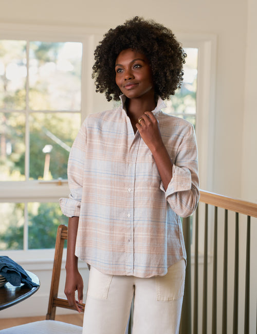 Woman wearing a plaid shirt and white pants standing in a room with large windows., front view