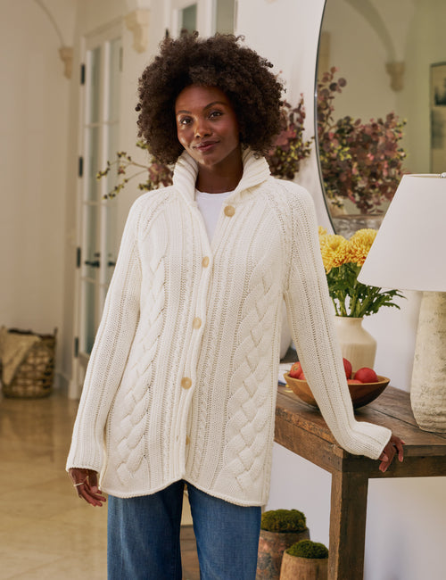 Woman wearing a white cable knit cardigan in a home setting, front view