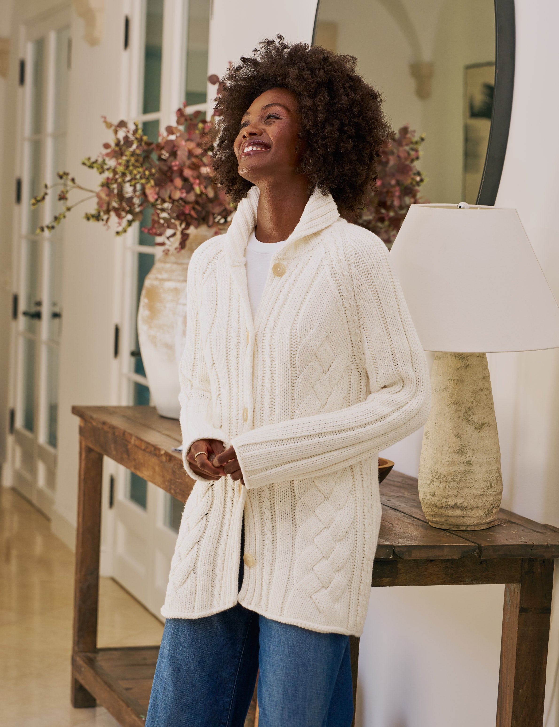 Woman wearing a white cable knit cardigan in a home setting
