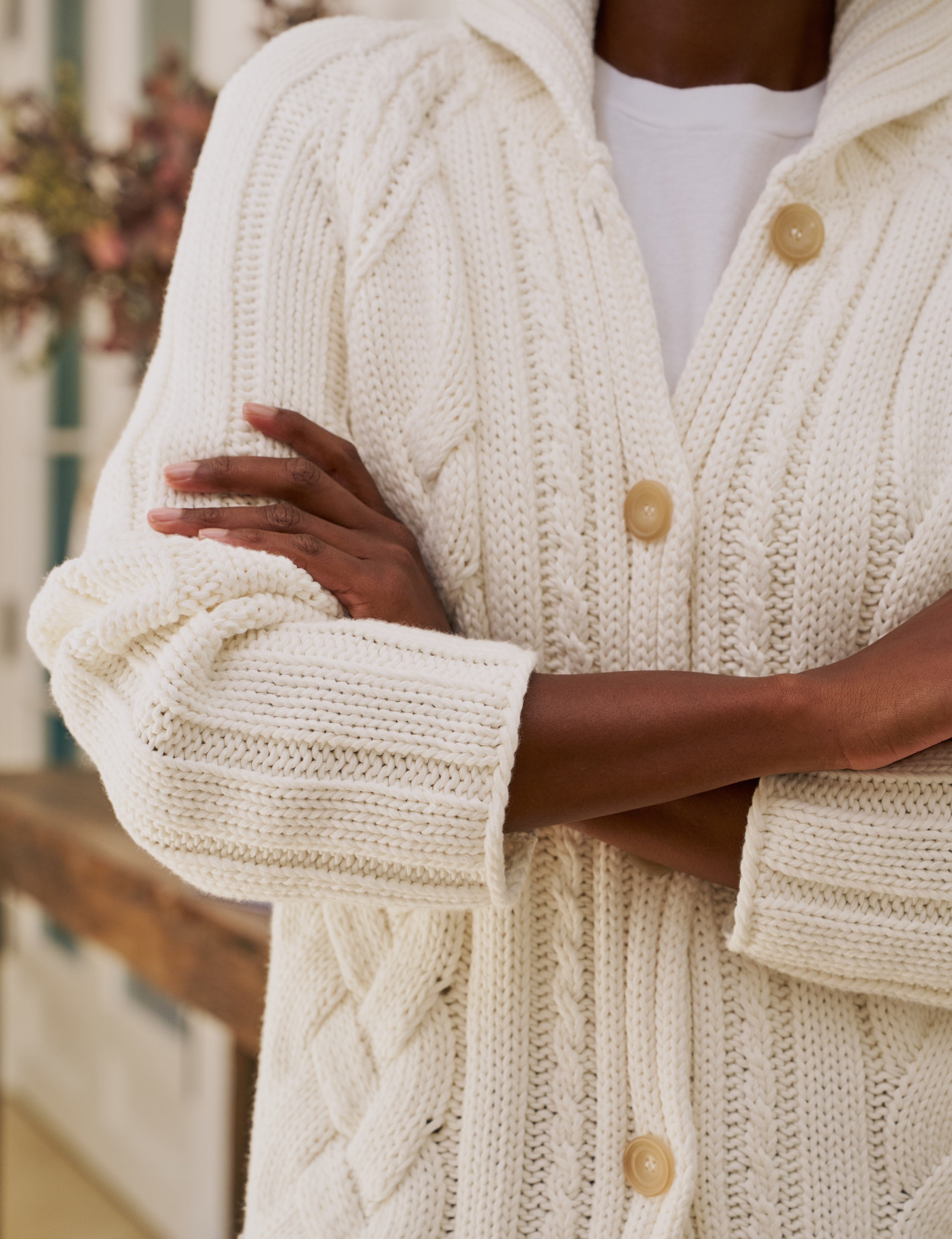Close-up of a person wearing a cream-colored knitted cardigan with horn buttons.