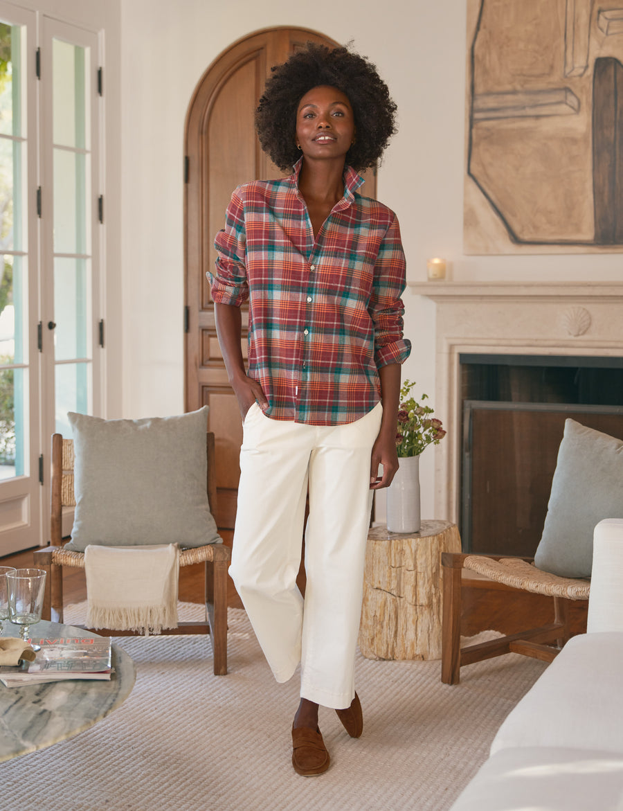 Woman standing in a living room wearing a plaid shirt and white pants.
