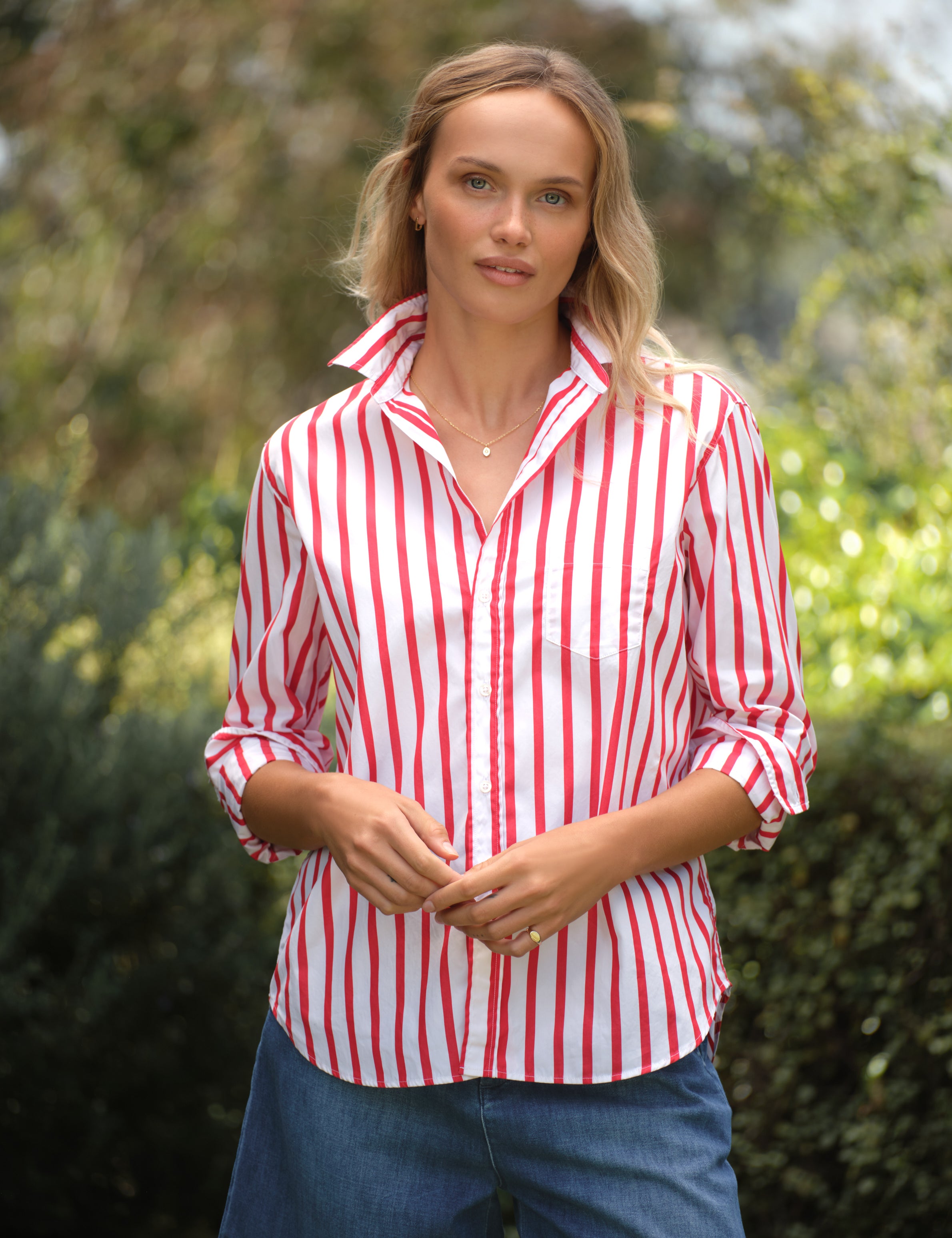 Woman wearing a red and white striped shirt outdoors with greenery in the background, front view