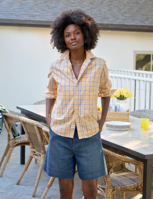 Woman standing outdoors on a patio with tables and chairs, front view