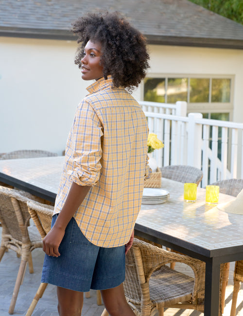 Woman standing on a patio with outdoor furniture and a house in the background, alternate view