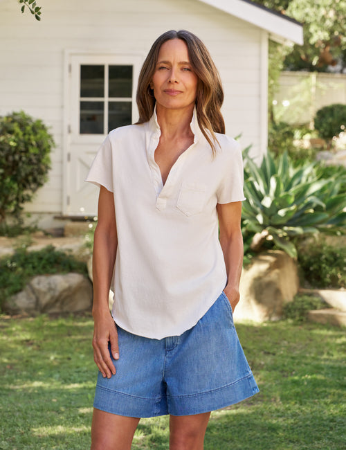 Woman wearing a white blouse and blue shorts standing outdoors in a garden., front view