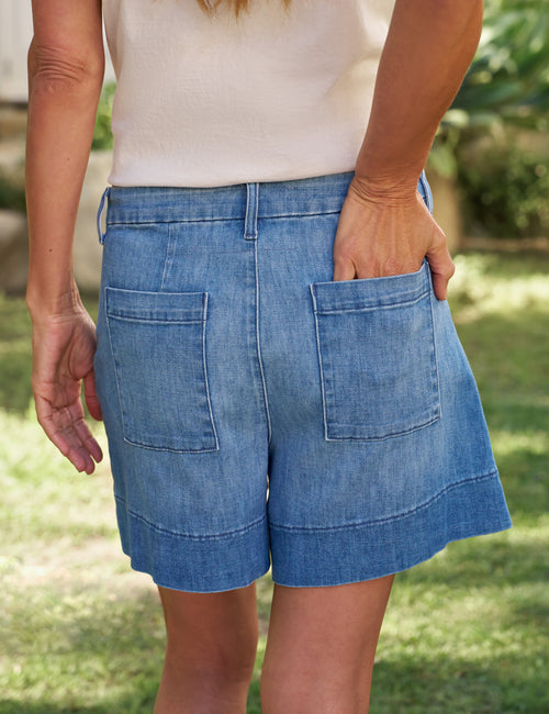 Person wearing blue shorts with a blurred natural background, alternate view