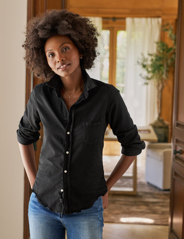 Woman wearing a black shirt and blue jeans standing in a room with wooden furniture and plants.