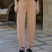 A person wearing tan drawstring pants with side seam detailing, paired with a black top and black loafers, standing on a stone patio.