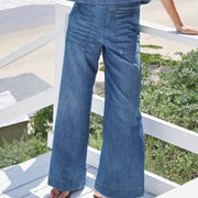 Woman in denim outfit standing on a deck overlooking a beach.