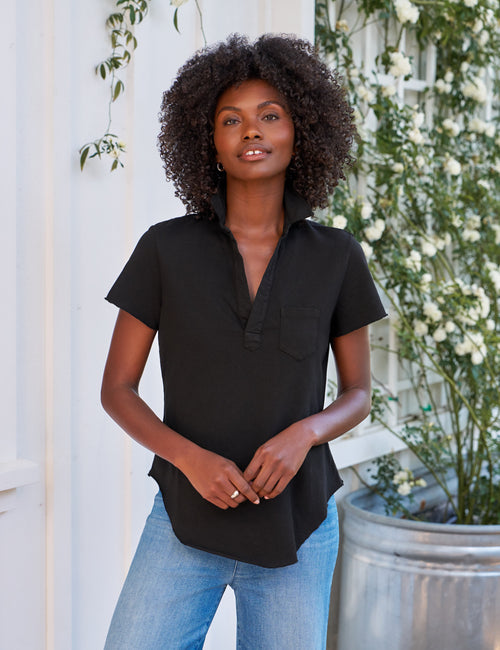 Woman wearing a black shirt and blue jeans standing in front of white flowers and greenery., front view