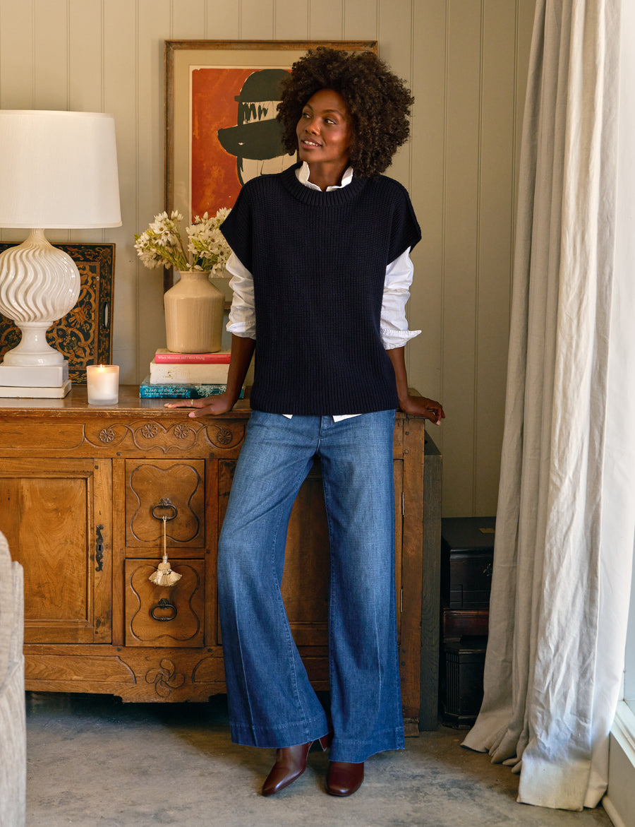 Woman standing in a room with a wooden cabinet and decorative items.