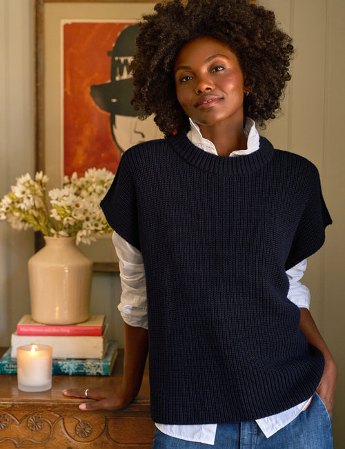 Woman wearing a navy sweater vest over a white shirt with a blurred background, front view