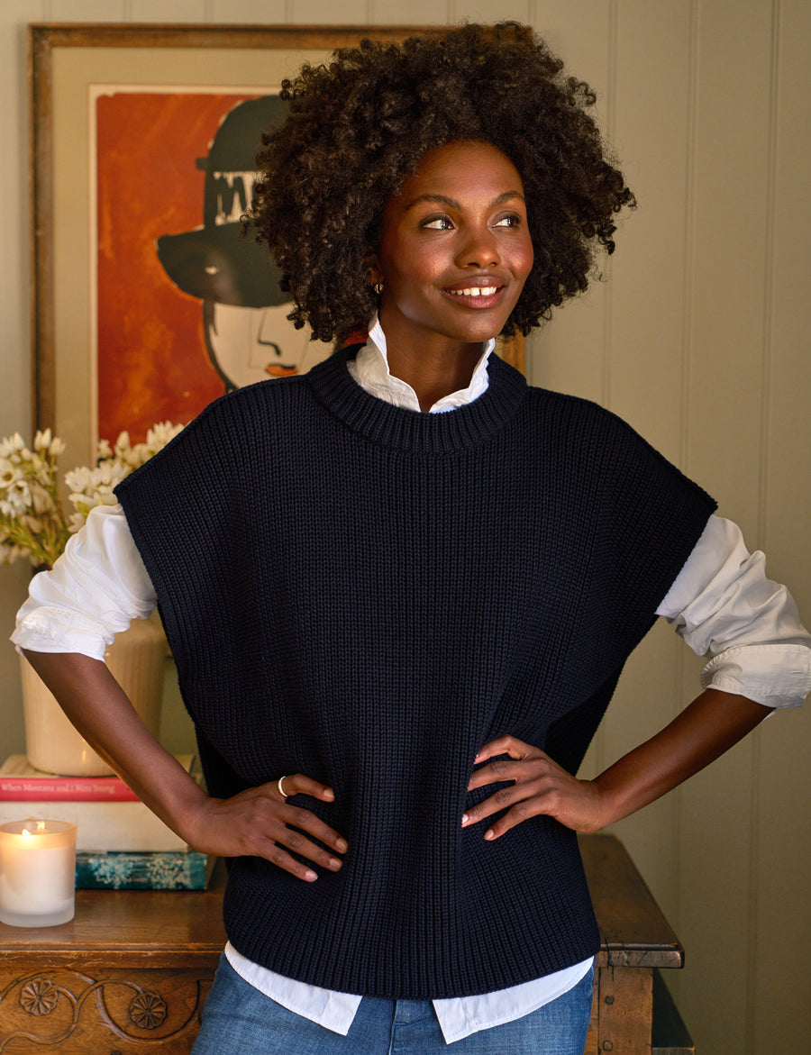 Woman wearing a navy sweater vest over a white shirt in a home setting.
