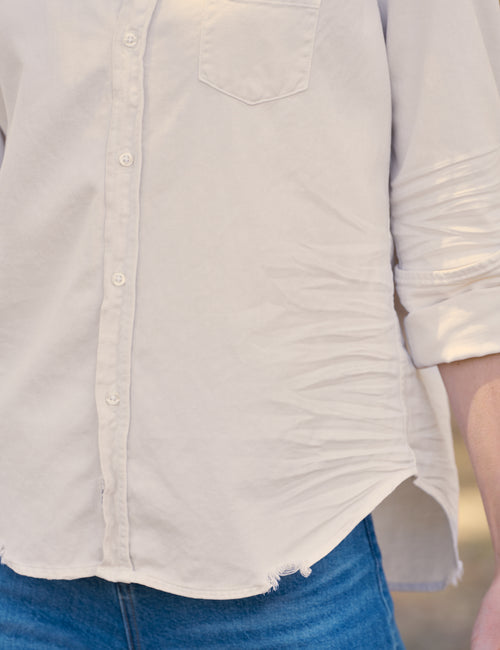 Close-up of a person wearing a white long-sleeve button-up shirt with rolled sleeves and blue jeans., view 3