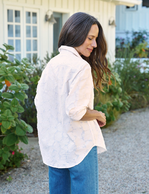 Woman wearing a light-colored blouse and blue jeans standing outdoors., alternate view